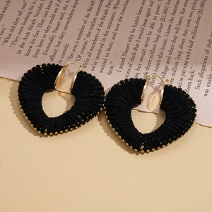 Close-up of black yarn-wrapped hollow heart hoop earrings on vintage newspaper background