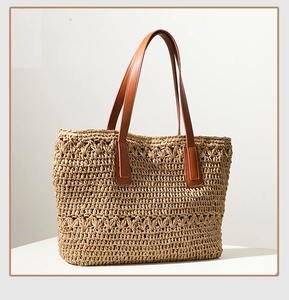Detail of woven straw tote bag featuring brown leather handles and intricate hollow pattern