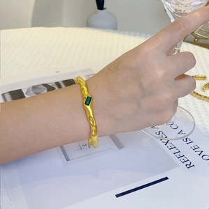 Detail showing irregular gold texture and green rectangular stone on a stainless steel cuff