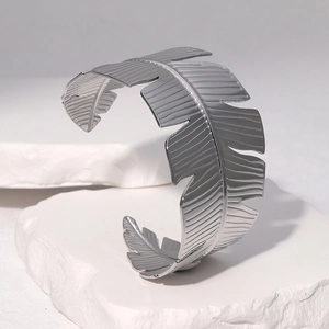 Silver palm leaf open cuff bracelet in stainless steel on a white stone background