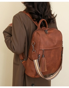 Brown vintage leather backpack featuring tassel charms and striped shoulder straps