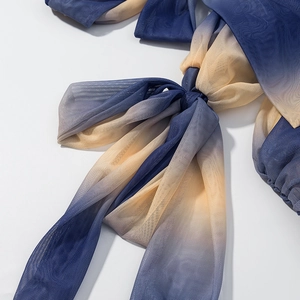 Detail aus blau-gelbem Mesh-Stoff mit Farbverlauf und Schleifendesign am langen Kleid