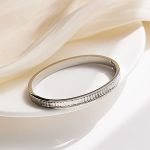 Close-up of a silver stainless steel bangle with trapezoidal crystals on a ceramic tray