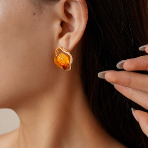 Détail d'une boucle d'oreille irrégulière en résine ambre avec monture dorée élégante