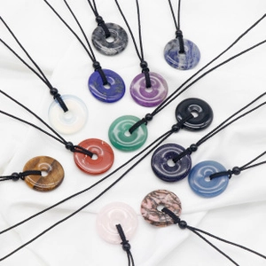 Close-up of assorted natural stone donut pendants with black cords on white fabric
