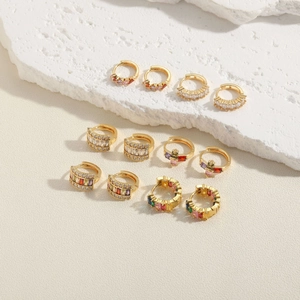 Set of gold huggie hoop earrings with colorful zircon stones on stone display