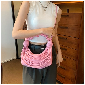Pink pleated handbag with knotted strap shown on model with white top and grey trousers