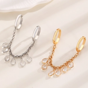 Detailed view of gold and silver chain earrings with crystal drops on white silk fabric