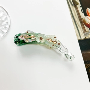 Macro shot of green floral banana clip featuring amber rhinestones on a smooth finish