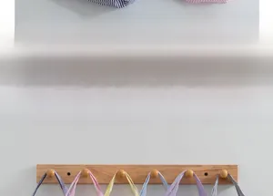 Detail of wooden wall-mounted rack with six hooks showing striped tote bags organization