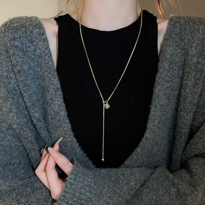 Detail of a gold-plated Y-shaped necklace with a sparkling rhinestone cube pendant on a model