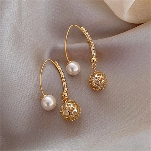 Detail of C-shaped gold pearl earrings with rhinestone sphere on grey silk fabric