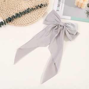 Detail view of a large grey silk bow hair clip on a minimalist lifestyle background