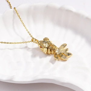 Close-up of golden koi fish pendant necklace resting elegantly in a white shell dish