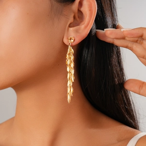 Close-up of long gold leaf tassel earrings with metallic fringe detail on model