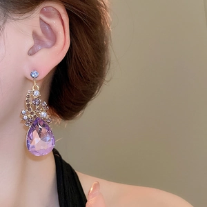 Close-up of elegant gold earrings with purple teardrop crystal on model side view