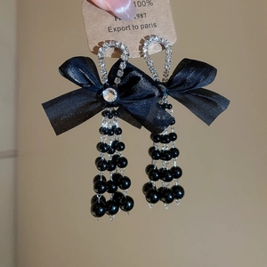 Close-up of black satin bow earrings with cascading bead tassels and rhinestone rings