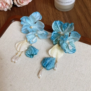 Detail of blue fabric flower earrings with pearl tassels on a rustic tray