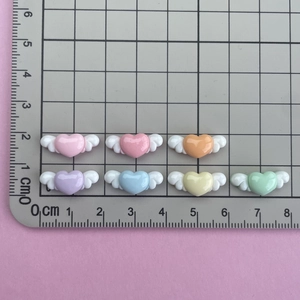 Flat lay of small winged resin hearts in seven colors showing 2.5cm size detail