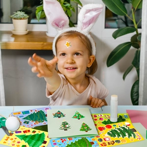 Close-up of child applying Christmas tree and gift box DIY stickers for holiday decor