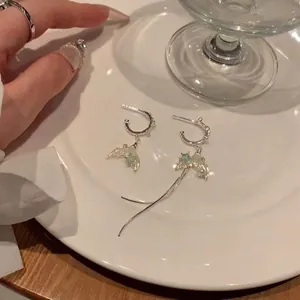 Asymmetric silver fish tail earrings with blue star accents and tassel on a white plate