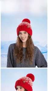 Detail view of red and white knit beanie with a large pom pom on a snowy mountain
