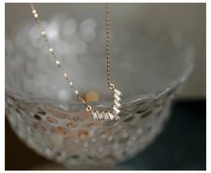 Artistic detail of gold V-shaped necklace with baguette zircon on textured glass
