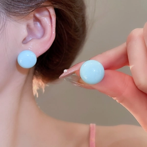Detailed close-up of light blue spherical stud earrings featuring a glossy resin finish