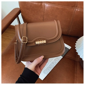 Gros plan d'un sac besace en cuir marron avec boucle dorée sur décor de journal vintage