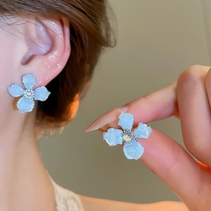 Detailed close-up of light blue 3D flower earrings with sparkling crystal center