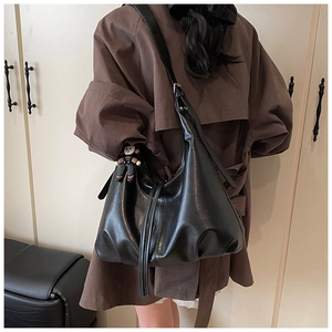 Black leather hobo bag side view with adjustable strap and cute plush doll charm