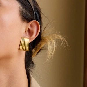 Close-up of elegant gold pleated textured stud earrings worn by a model in warm light