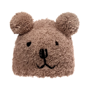 Close-up of brown plush bear hat with fluffy pom-poms and cartoon embroidery detail