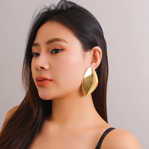 Primo piano di una modella che indossa grandi orecchini geometrici dorati opachi