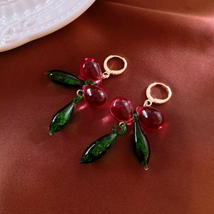 Vintage cherry drop earrings with red and green glass beads on gold hooks over satin