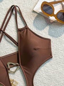 Detail of dark brown swimsuit with gold heart buckle and chains on woven texture