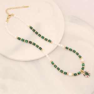 Collana di pietre verdi e perle con ciondolo a fiore dorato su vassoio bianco