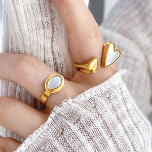 Dettaglio di anelli d'oro con inserti in madreperla a cuore e ovale su maglia bianca