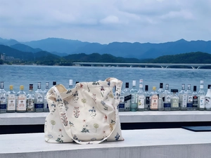 Floral print cotton tote bag with wide straps shown against a scenic outdoor background
