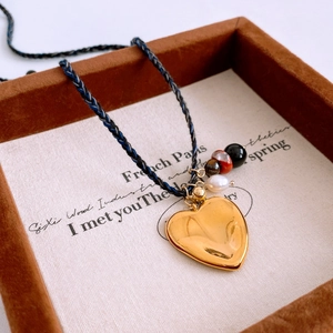 Détail d'un pendentif cœur doré avec perles et billes colorées sur collier en corde