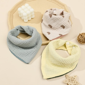 Detailed flat lay of three soft cotton gauze baby bibs in assorted pastel colors and patterns