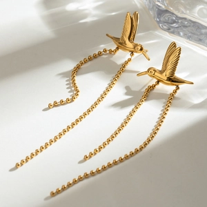 Detailed close-up of gold hummingbird earrings with delicate hanging bead tassels
