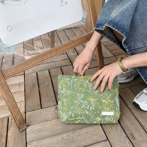 Close-up of green cotton linen pouch with delicate yellow flower embroidery and brand tag