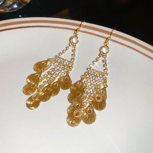 Close-up of gold leaf tassel earrings with sparkling rhinestones in a white ceramic dish