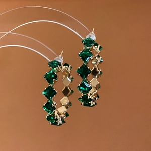 Close-up of golden hoop earrings featuring emerald green square-cut crystals and elegant design
