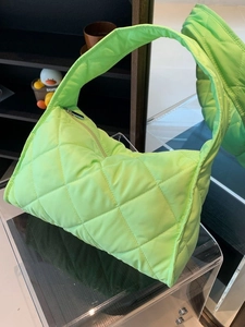 Fluorescent green quilted nylon tote bag with zipper closure on acrylic stand