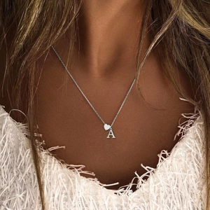 Silver alphabet letter A necklace with mini heart pendant worn by a model on collarbone