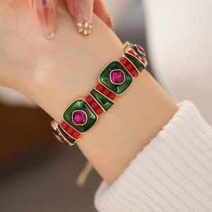 Close-up of vintage gold bracelet with green enamel and red gems on a model wrist