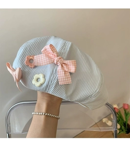 Close-up of light blue beret with pink plaid bow and flower on textured fabric
