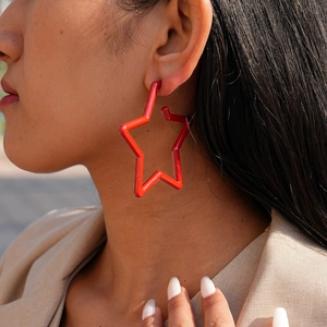 Close-up of a model wearing large red hollow star earrings in minimalist enamel finish